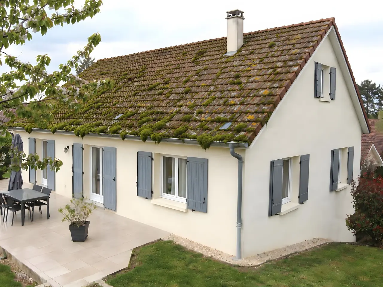 Maison blanche au toit de tuiles rouges couvert de mousse verte, avant nettoyage
