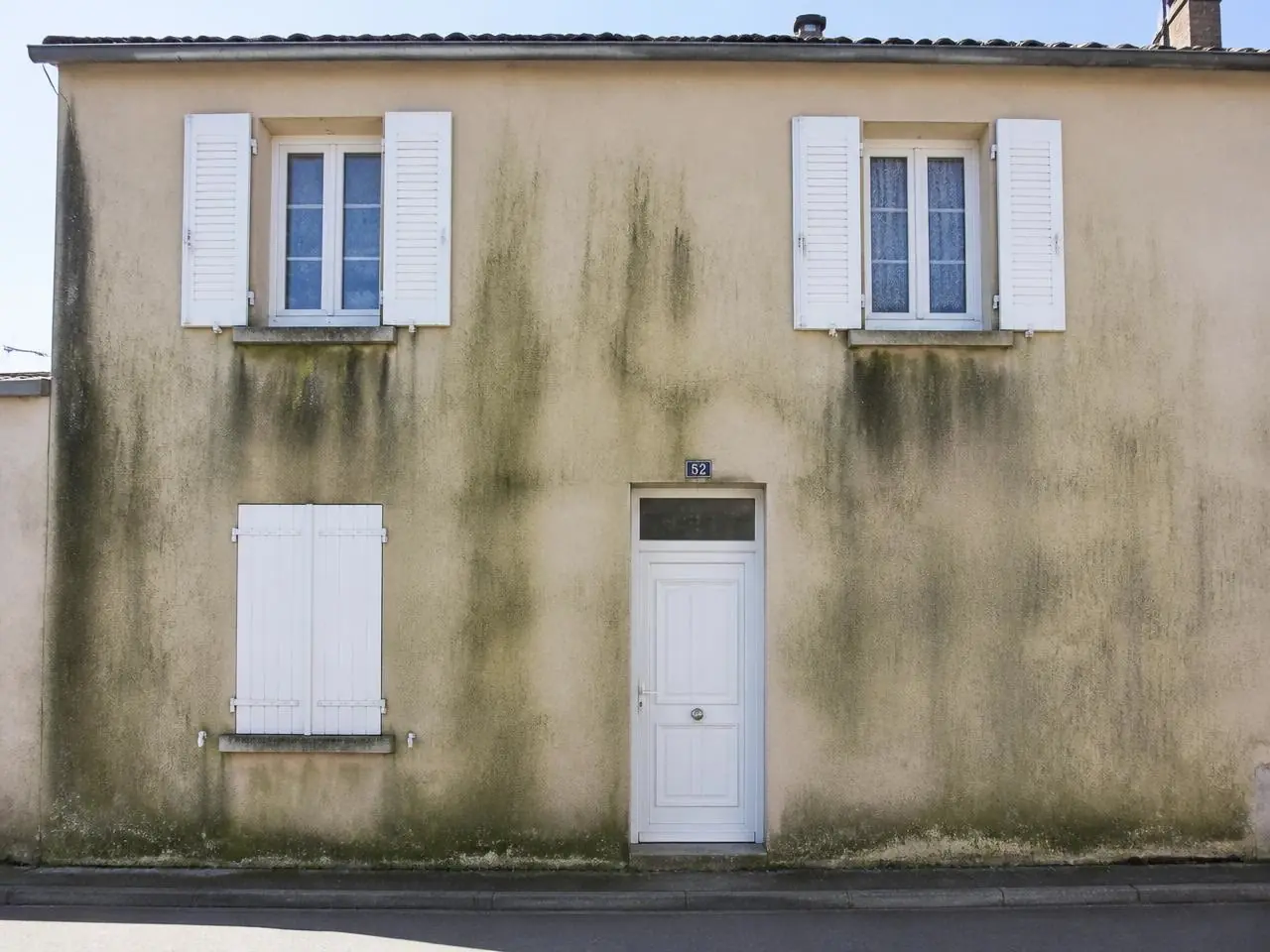 Façade sur rue à l'enduit beige couverte de coulures vertes et noires, avant nettoyage