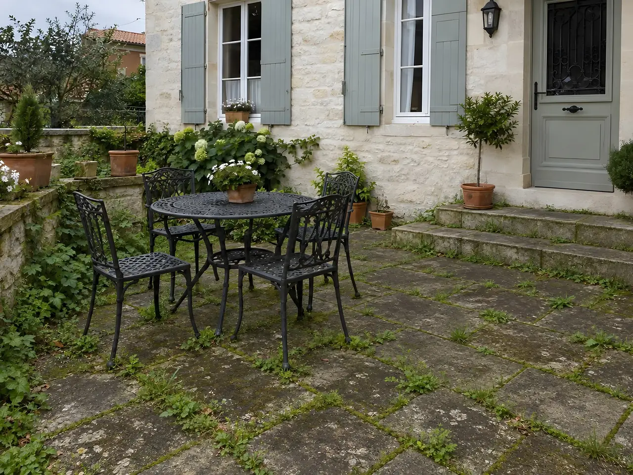 Terrasse dallée devant une maison en pierre, dalles noircies et joints moussus